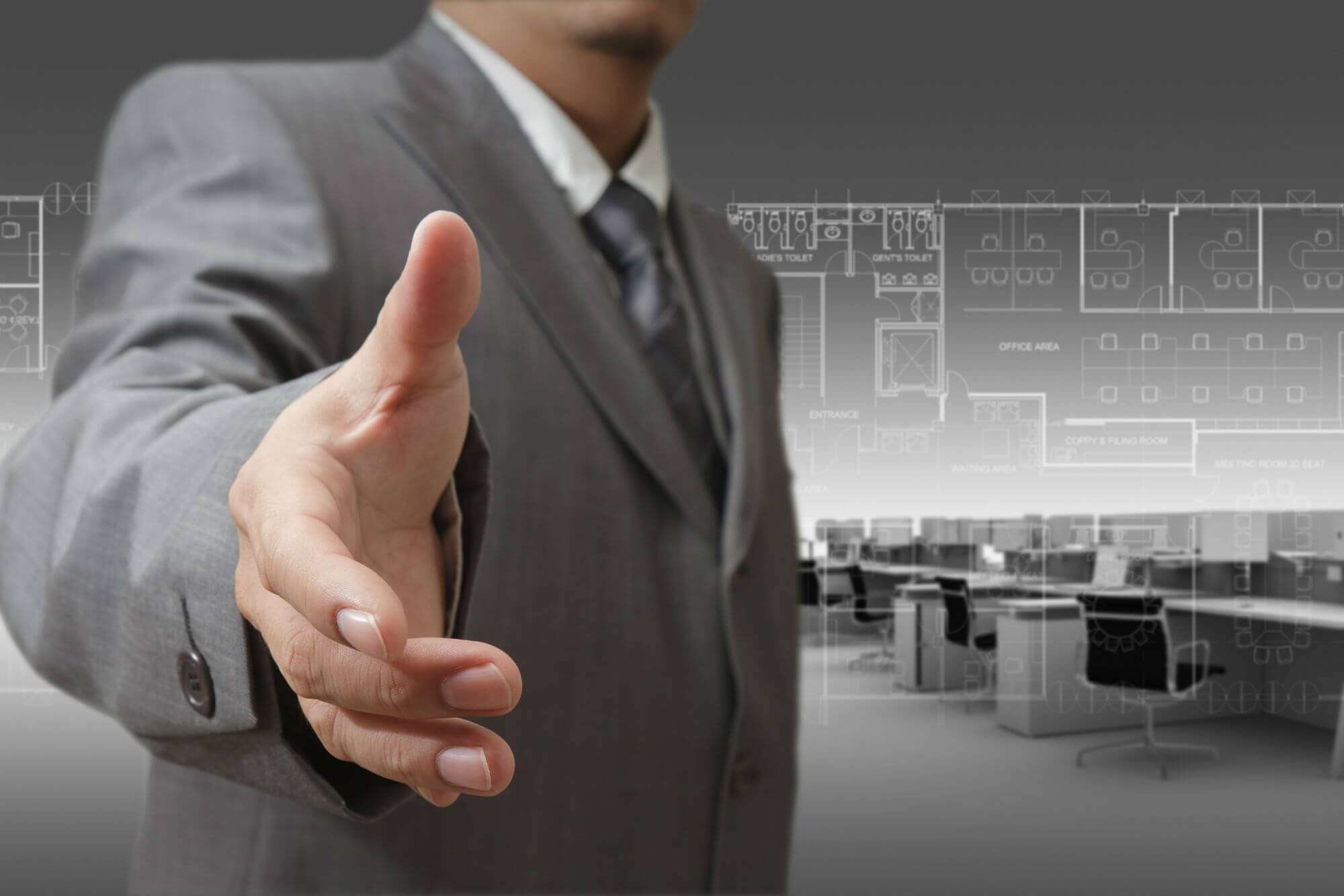 A man in a suit extends his hand for a handshake against a backdrop of office blueprints and an open-plan office, conveying professionalism and partnership.